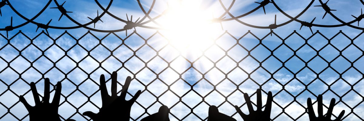 Stock image showing silhouette of handcuffed hands behind barbed wire