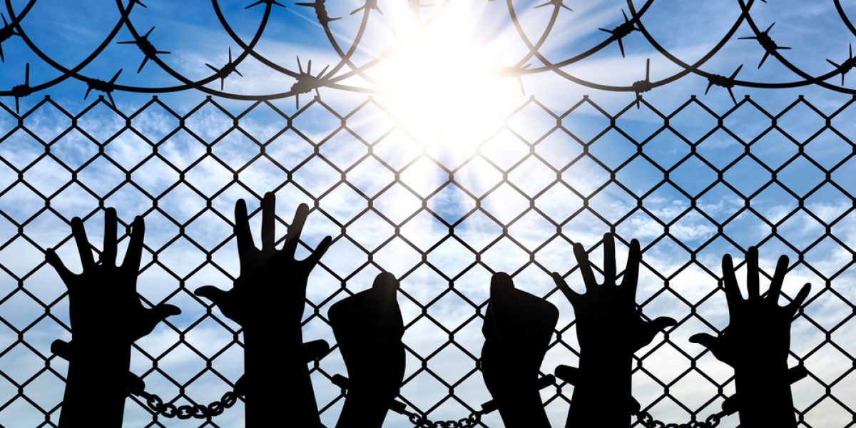 Stock image showing silhouette of handcuffed hands behind barbed wire