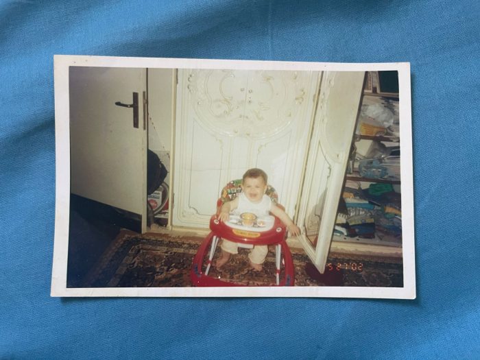 One of Batoul's baby photos, saved from her house in Gaza moments before the family were forced to flee. Shared with permission from Batoul. Batoul is in the centre of a room, in a baby walker and high chair, with a bowl of food in front of her. Batoul is laughing.